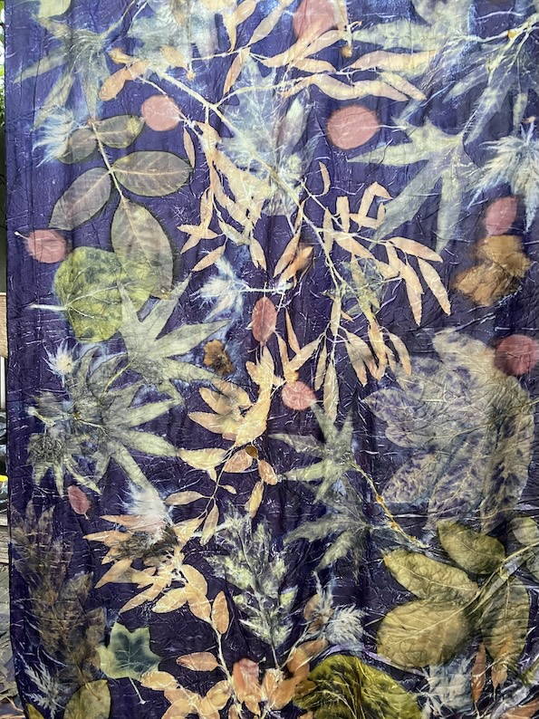 Een kleurrijke stof bedekt met een botanisch ontwerp van bladeren en takken op een donkere achtergrond.